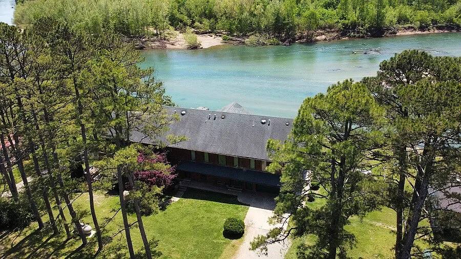 Aerial view of the main riverfront lodge on 700 feet of spring-fed crystal-clear Current River in Doniphan, Missouri. Surrounded by tall pine trees, this private luxury estate includes 20 acres, a wraparound porch, and direct access to world-class fishing, boating, and nature trails.